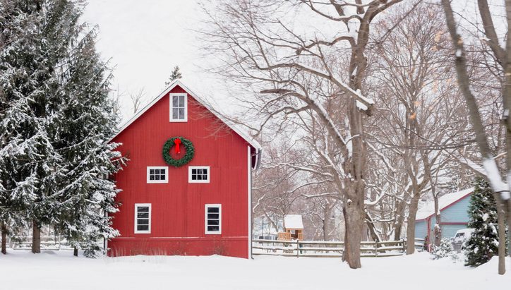 Red barn with a holiday wreath surrounded by snow