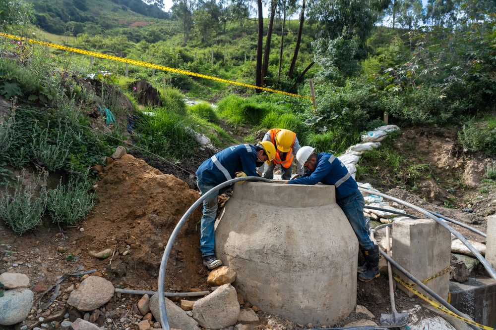 Crew installing a concrete septic tank on a rural hillside