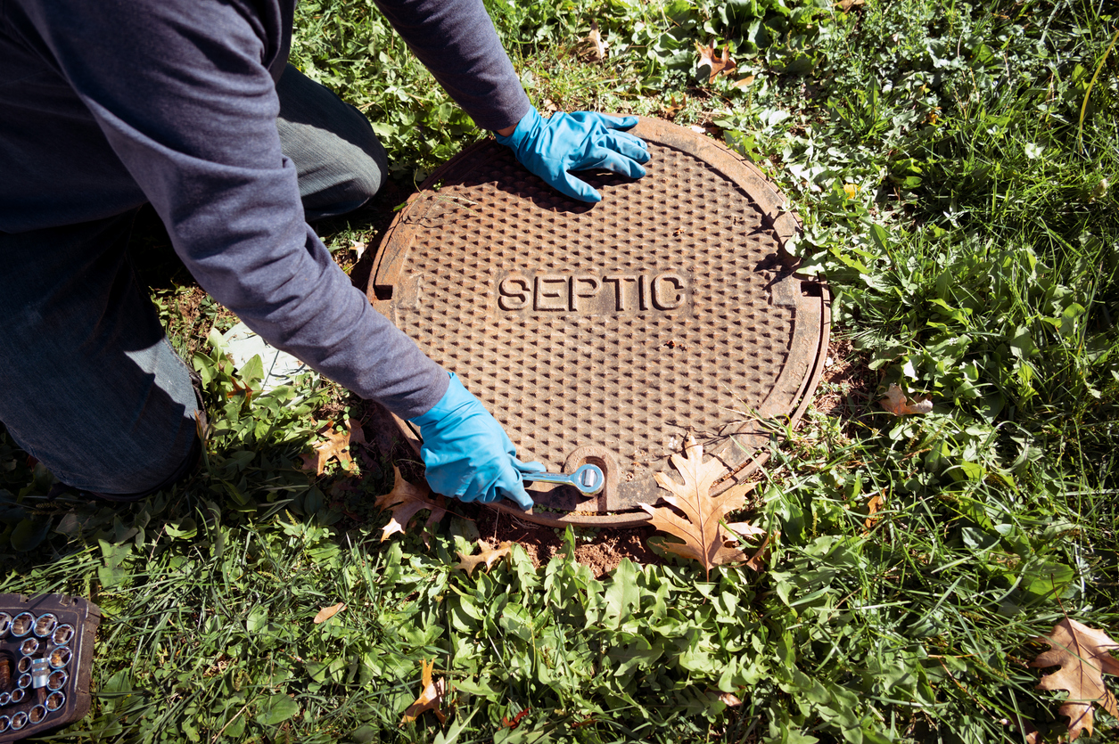 Technician unbolting a cast-iron lid marked SEPTIC to open the tank