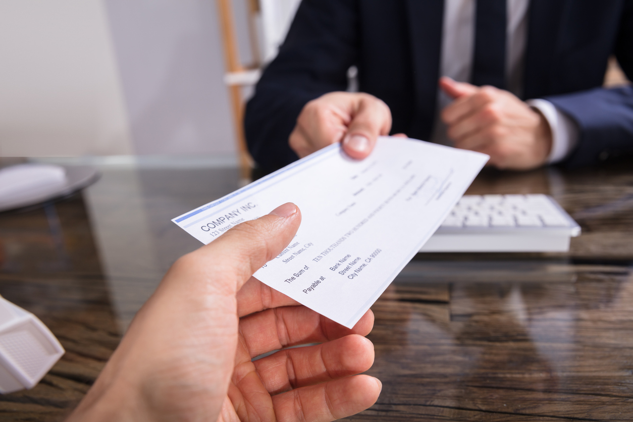 Two hands exchange a check across a desk. One person wears a suit.